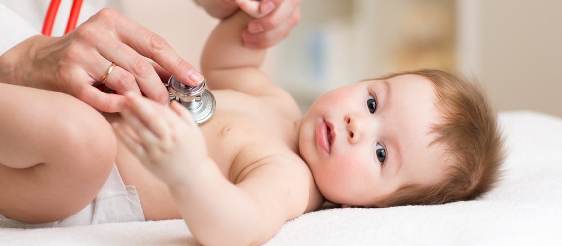 Pediatrician examining three months old baby. Doctor using a stethoscope to listen to kid chest checking heart beat