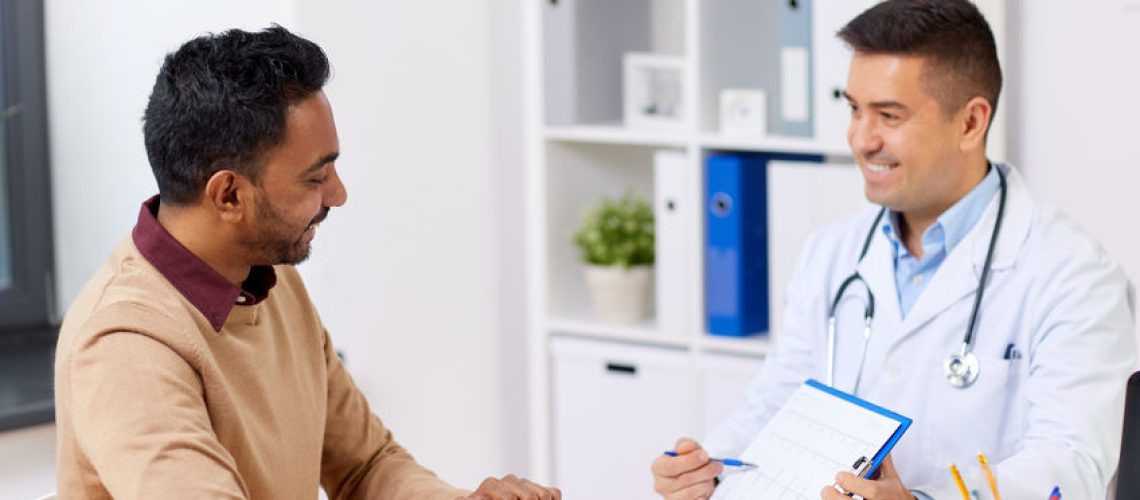 medicine, healthcare and people concept - happy doctor with cardiogram and young male patient meeting at hospital