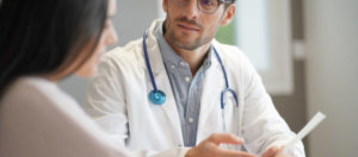 Modern young doctor speaking to patient in office