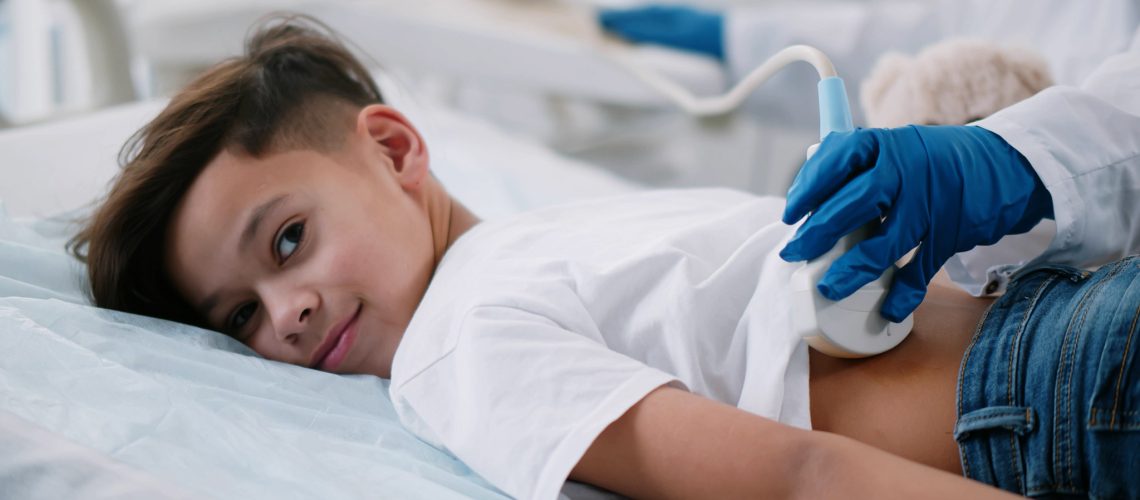 Close up of doctor performing kidney ultrasound scan on preteen african boy. Medical specialist examining child back with sonogram equipment in clinic office