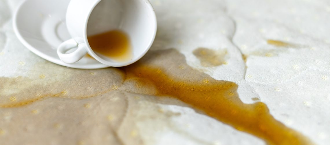 Spilled coffee on the bed. Unlucky, unfortunate breakfast. Accidentally dropped cup with saucer on white bedsheet. Wet spot.